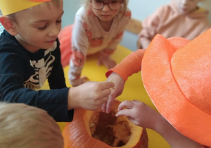 Na zdjęciu widać dzieci które wydrążają dynię. Zabawa sensoryczna.