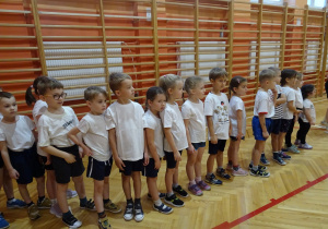Na zdjęciu widać dzieci które stoją na sali gimnastycznej i czekają na zawody sportowe.
