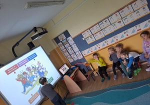 Na zdjęciu widać dzieci które pracują na tablicy multimedialnej i rozwiązują zadania związane z karnawałem.