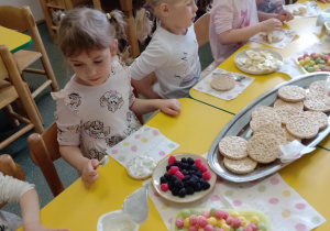 Na zdjęciu widać dziecko które układa kompozycję kwiatową na wafelkach według własnego pomysłu.