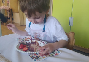 Na zdjęciu widać chłopca który je sałatkę owocową.