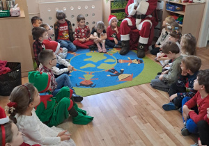Na zdjęciu widać dzieci i Św Mikołaja który wręcza prezenty.