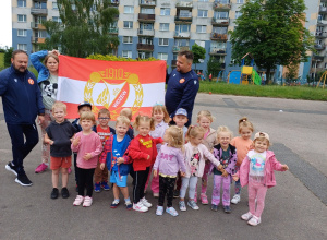 Grupa dzieci stoi w gromadce w tle flaga z herbem Łódzkiego Widzewa