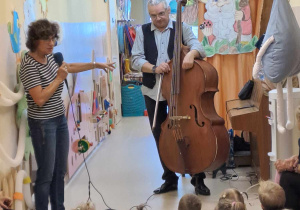 Na zdjęciu widać Pana który gra na kontrabasie i Panią oraz dzieci które oglądają koncert