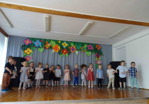 Szesnastka dzieci stoi na scenie w jednym szeregu.
