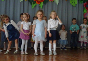 Cztery dziewczynki stoją na scenie recytując wierszyk. Dziewczynka w okularach stojąca po lewej stronie drapie się po kolanie. Dziewczynka po prawej stronie poprawia kosmyk włosów na twarzy.
