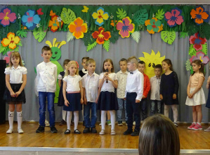 Dzieci w strojach galowych stoją na scenie. Szóstka dzieci w pierwszym rzędzie mówi do mikrofonu.