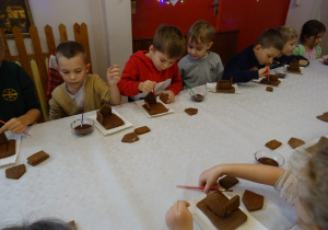 Na zdjęciu widać dzieci na warsztatach domek z piernika. Dzieci składają i ozdabiają domek.