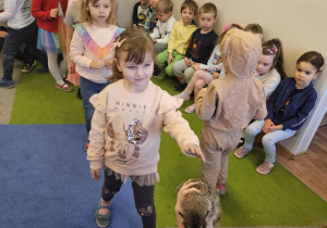 Na zdjęciu widać dziewczynkę która stoi w kolejce do pogłaskania surykatki.