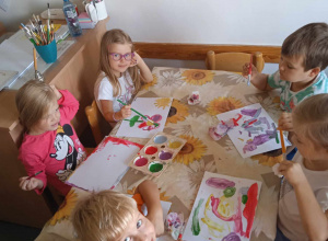 Czworo dzieci siedzi przy stoliku i maluje farbami