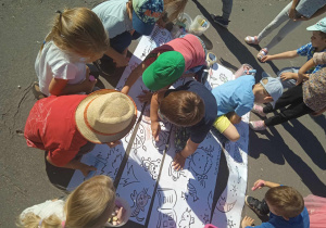 Dzieci wspólnie kolorują duża kolorowankę rozłożoną na podwórku przedszkolnym