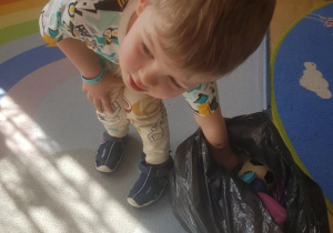 Na zdjęciu widać chłopca który szuka w worku przedmiotów sensorycznych.