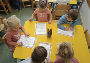 Dzieci siedzą przy żółtym stoliku i wykonują kartę pracy