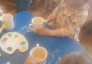 Na zdjęciu widać dzieci które malują kubki farbami na warsztatach ceramicznych.