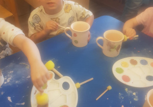 Na zdjęciu widać dzieci które malują kubki farbami na warsztatach ceramicznych.