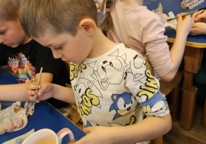 Na zdjęciu widać dzieci które malują kubki farbami na warsztatach ceramicznych.