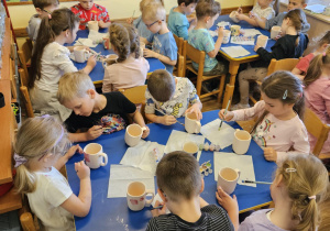 Na zdjęciu widać dzieci które malują kubki farbami na warsztatach ceramicznych.
