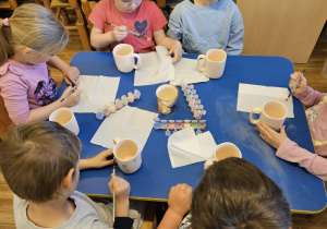 Na zdjęciu widać dzieci które malują kubki farbami na warsztatach ceramicznych.