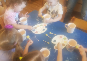 Na zdjęciu widać dzieci które malują kubki farbami na warsztatach ceramicznych.