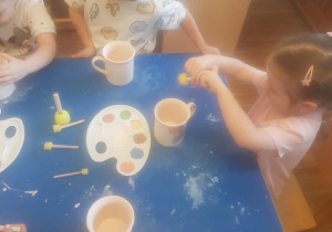 Na zdjęciu widać dzieci które malują kubki farbami na warsztatach ceramicznych.
