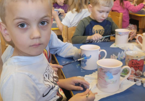 Na zdjęciu widać dzieci które malują kubki farbami na warsztatach ceramicznych.