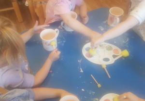 Na zdjęciu widać dzieci które malują kubki farbami na warsztatach ceramicznych.