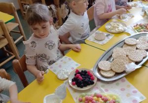 Na zdjęciu widać dziecko które układa kompozycję kwiatową na wafelkach według własnego pomysłu.