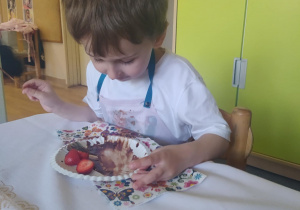 Na zdjęciu widać chłopca który je sałatkę owocową.