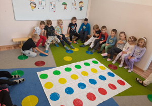 Na zdjęciu widać dzieci które wykonują zadania na macie w kropki.