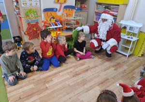 Na zdjęciu widać dzieci i Św Mikołaja który wręcza prezenty.