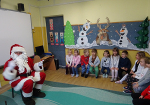 Na zdjęciu widać dzieci i Św Mikołaja który wręcza prezenty.