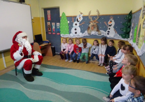 Na zdjęciu widać dzieci i Św Mikołaja który wręcza prezenty.