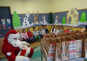 Na zdjęciu widać dzieci i Św Mikołaja który wręcza prezenty.