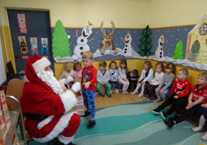 Na zdjęciu widać dzieci i Św Mikołaja który wręcza prezenty.