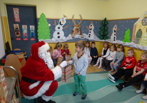 Na zdjęciu widać dzieci i Św Mikołaja który wręcza prezenty.
