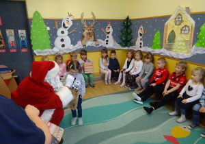 Na zdjęciu widać dzieci i Św Mikołaja który wręcza prezenty.