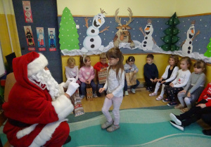 Na zdjęciu widać dzieci i Św Mikołaja który wręcza prezenty.