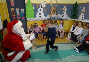 Na zdjęciu widać dzieci i Św Mikołaja który wręcza prezenty.