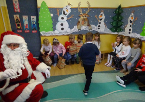 Na zdjęciu widać dzieci i Św Mikołaja który wręcza prezenty.