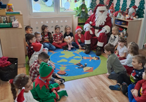 Na zdjęciu widać dzieci i Św Mikołaja który wręcza prezenty.