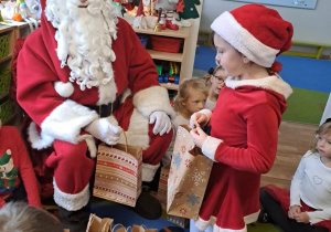 Na zdjęciu widać dzieci i Św Mikołaja który wręcza prezenty.