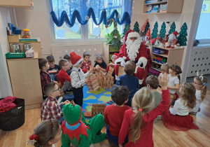 Na zdjęciu widać dzieci i Św Mikołaja który wręcza prezenty.