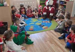 Na zdjęciu widać dzieci i Św Mikołaja który wręcza prezenty.