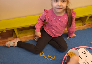 Na zdjęciu widać dziewczynkę która pisze literę y,Y z makaronu.