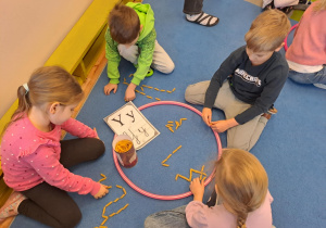 Na zdjęciu widać dzieci które piszą literę y,Y z makaronu.