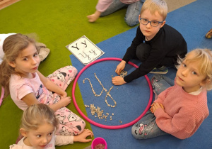 Na zdjęciu widać dzieci które piszą literę y,Y z makaronu.