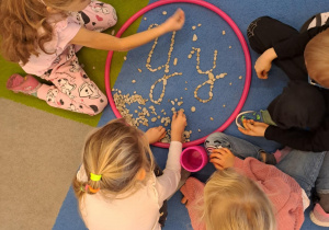 Na zdjęciu widać dzieci które piszą literę y,Y z makaronu.