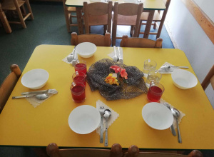 Żółty stolik a na nim sześć białych talerzy i ozdoba na środku stołu kwiatki i świeczka
