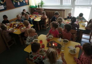 Na zdjęciu widać cztery stoliki przy każdym siedzi szescioro dzieci, dzieci mają w miseczkach wlaną zupę, którą jedzą.