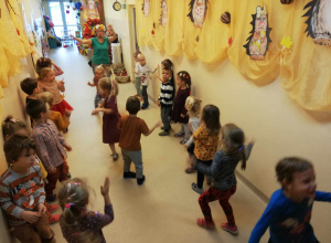 Dzieci w holu przedszkola tańczą, naśladują panią w zielonej bluzce z jesiennym wiankiem na głowie